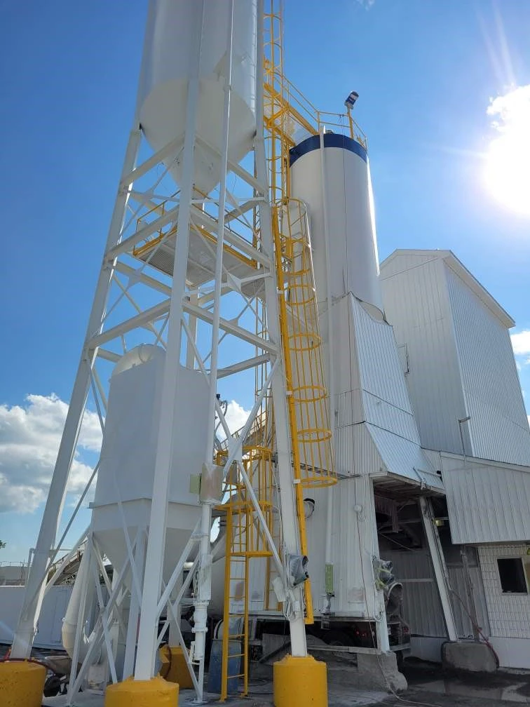 Storage silos and yellow access ladders at a CBM ready-mix concrete plant.