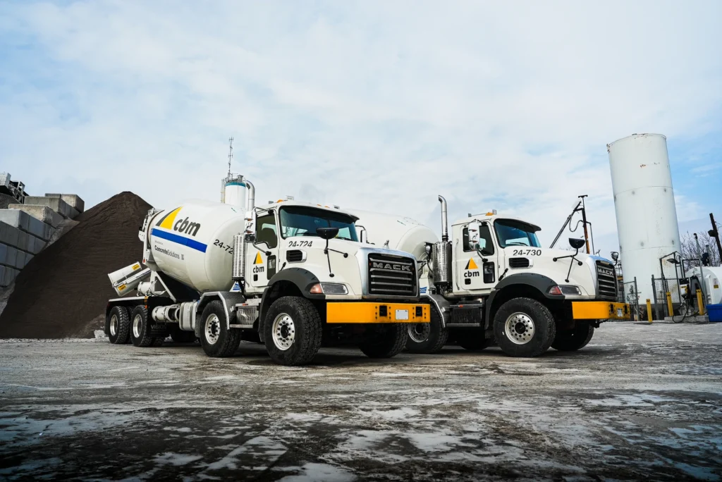 Two CBM ready-mix concrete trucks parked at a concrete plant.